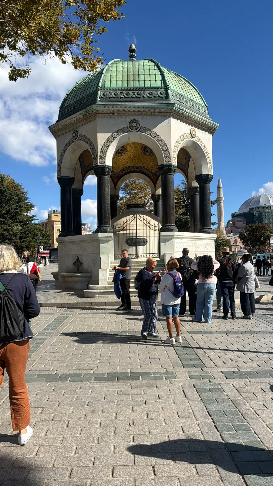 Tour guests at the German Fountain in Sultanahmet Square with the Blue Mosque minarets behind, Istanbul